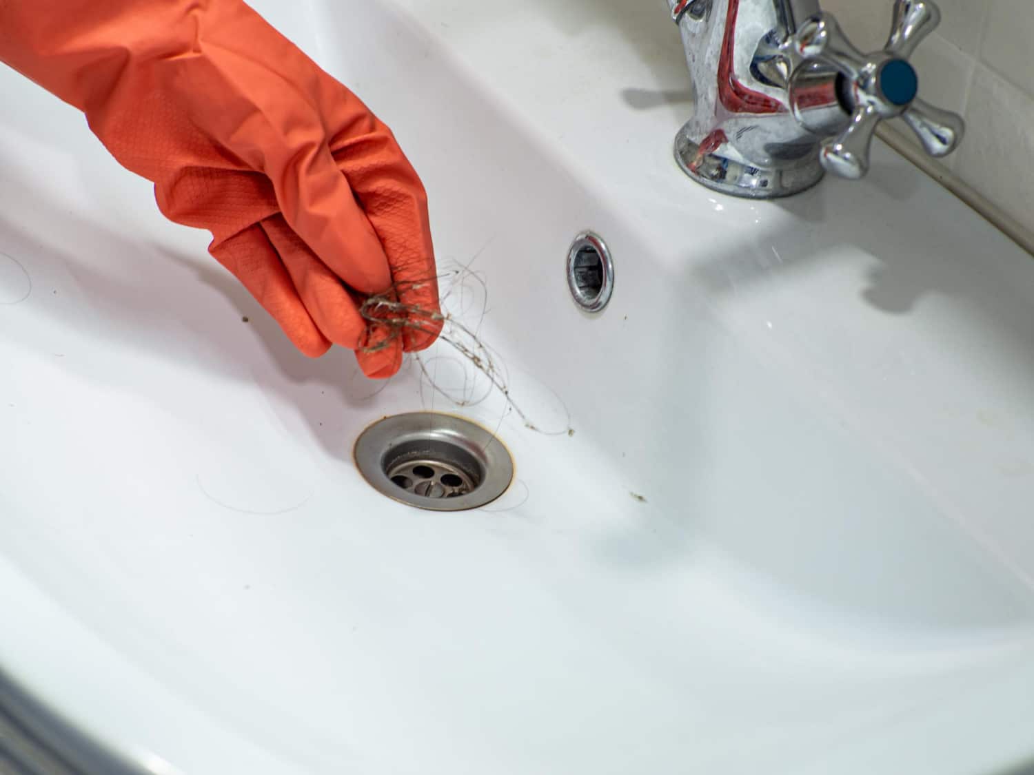 Une personne équipé d'un gant tenant des résidus de cheveux en train de déboucher un lavabo